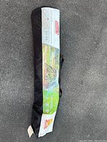 Photo of the Coleman Instant Screenhouse tent packed in its black carrying bag with label showing tent image and brand.