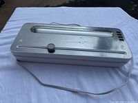 Top view showing the vacuum sealer's transparent window, control buttons, and knob with power cord visible.
