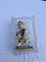 Bobblehead in original plastic packaging showing front pose with player holding football, wearing green and yellow Packers uniform.