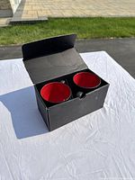 Set of two black ceramic cups with red interiors in black cardboard box, outdoor photo with clear sunlight