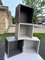 Four cube-shaped locker cabinets stacked with white and gray colors visible, shown outdoors on a white cloth surface.