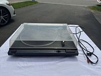 JVC L-AX3B turntable with clear plastic dust cover, visible RCA cables, setup on white cloth outside.