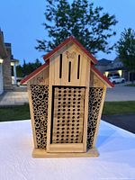 Front view of wooden butterfly house showing red roof trim, multiple holes and bamboo tube clusters on either side, decorative butterfly cutouts.