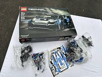 Photo of LEGO Technic McLaren Racing set in box with unassembled pieces in plastic bags and sticker sheet visible.