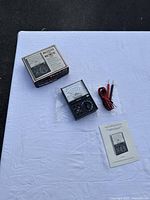 Micronta 22-201U multimeter, test leads, instruction manual, and original box on white cloth surface.