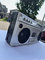Side angle view showing silver body, black speaker grille and volume and tone control knobs.