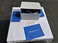 Sony PlayStation VR headset in original box with cables and user manual on a white cloth surface outdoors.