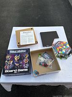 Photo showing Bibleman board game box, opened box with game pieces including dice and cards, instruction sheet, hexagonal game board on table.