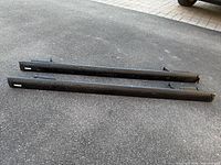 Two black metal Thule roof rack crossbars side by side on ground showing Thule logos and condition.