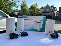 Three TP-Link Deco M4 Wi-Fi mesh units with power adapters displayed outdoors on a table with product box in background