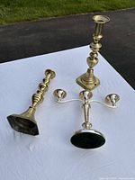 Three vintage candlesticks including two upright bronze single holders and one silver-toned triple holder viewed outdoors