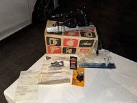 Full view of the WEN 931 electric plane placed on its original box along with manual, faceplate, and additional accessories on white table.