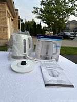 Photo of white Westinghouse electric kettle with base, instruction manual, and warranty manual on a white cloth outdoor setup, along with the product box.
