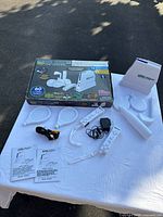 Wireless 60 game console with main unit, controller, sports accessories (rackets and arm attachments), cables, power adapter, instruction manuals laid on table with original box showing wear in background