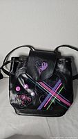 Front view of black faux leather Descendants backpack showing colorful stripes, purple heart on flap, and pins.