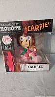 Front view of the Handmade By Robots Carrie Knit Series collectible vinyl figure in original packaging showing the figure with button eyes and yarn knit aesthetics, new in box.