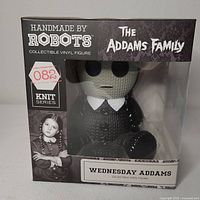 Front view of box showing Handmade By Robots branding, The Addams Family logo, Knit Series tag and Wednesday Addams figure visible in box.