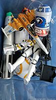 Blue container with assorted Star Wars toys including Stormtrooper figure, BB-8, yellow X-Wing Starfighter, R2-D2-themed electronic device.