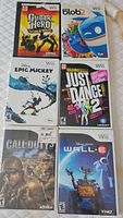 Top view of 6 Nintendo Wii game cases including Guitar Hero World Tour, de Blob 2, Disney Epic Mickey, Just Dance 2, Call of Duty World at War, WALL-E