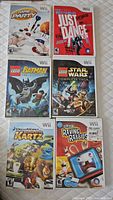 Top view of five Wii game cases: Game Party, Just Dance, LEGO Batman, LEGO Star Wars Complete Saga, DreamWorks Madagascar Kartz, and Rayman Raving Rabbids.