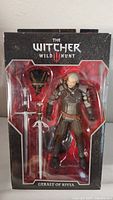 Front view of The Witcher 3 Wild Hunt Geralt of Rivia action figure in original box with visible sword and monster head accessories.