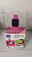 Front view of Kidizoom Smart Watch DX2 in pink inside clear display packaging showing product and box front with kid images and branding