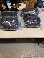 Four navy blue Jeadvia sleeping bags in individual carrying cases placed on a table.