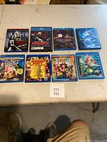 Blu-ray movie lot showing 8 titles laid out on table: Sin City, War Zone The Punisher, The Nightmare Before Christmas, Avatar, The Sting, Sausage Party, Toy Story 3, The Little Mermaid.
