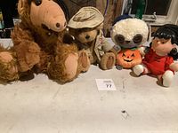 Four stuffed animals including ALF, teddy bear, plush sloth with pumpkin, and vintage doll.
