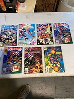 Seven Marvel comic books laid flat on table; titles include Slingers, X-Factor, Guardians of the Galaxy, Nomad, Spider-Man, Avengers