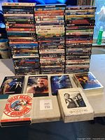 Large stack of DVD cases with diverse movie titles shown from front and side, including familiar movies and series cases.