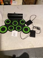 Top view of electronic drum mat with green circle pads and two power adapters.