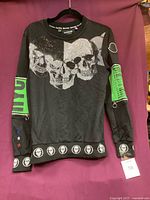 Front view of black sweatshirt with skull print and green zipper detailing on sleeves.