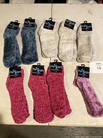 Photo showing eight pairs of new Hot Steps fuzzy socks in blue, white, pink, and purple colors laid out on table.