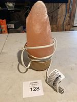 Pink Himalayan salt lamp with wooden base and white power cord wrapped around the base on a table.