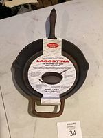 Cast iron skillet with original Lagostina branding paper showing front view, placed on white surface.