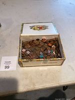 Open cigar box showing a heavy collection of old pennies with oxidation and wear.
