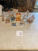 Full view of 10 assorted perfume bottles on a table, various shapes and colors visible including orange, blue, clear and amber.