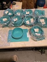Ten new blue Modaliv bowls wrapped in plastic on a table, along with a placemat and one unwrapped bowl in front.
