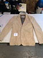 Front view of a light tan/beige women's suede jacket laid flat on a white surface, showing full length and sleeves.