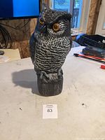 Front view of black and white owl figurine sculpture with bright yellow eyes, on a light surface inside a room