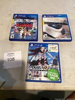Three PS4 game cases: Katamari Power, Star Wars Battlefront, and Akiba's Trip on a table with seller lot number card next to them.