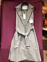 Gray sleeveless vest-style outerwear hanging on black hanger against purple background.