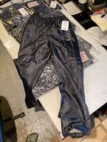 Full view of one black pair of Sports-Life pants on top of plastic packaging containing other pairs.