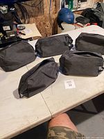 Five grey fabric travel shaving bags on white table, arranged spread out to show front and side angles.