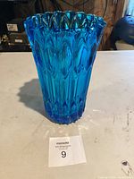 Blue glass vase standing upright on a white surface, showing its height and textured surface.