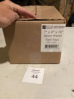 Closed cardboard box labeled Atlas Paper Bag, 7" x 4" x 10" Brown Waxed Sani Sacs, 500 per case