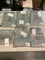 Six pairs of new women's grey sweat pants packaged in plastic with size tags visible, laid out on a table.