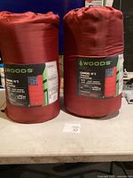 Two new red Woods Canmore sleeping bags packaged in their compression sacks with visible labels.