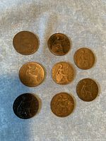 Photo showing nine British half penny coins of various dates including 1887 and 1921, laid on a grey cloth surface.